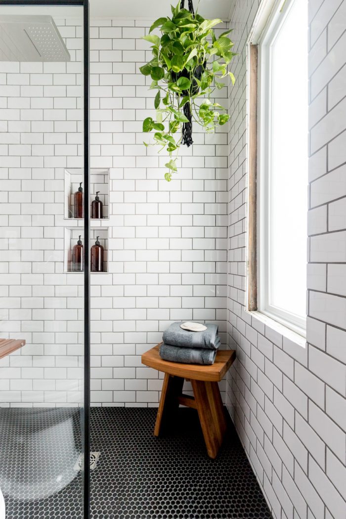 White subway tile in a small bathroom with gray towels on a wooden stool. 