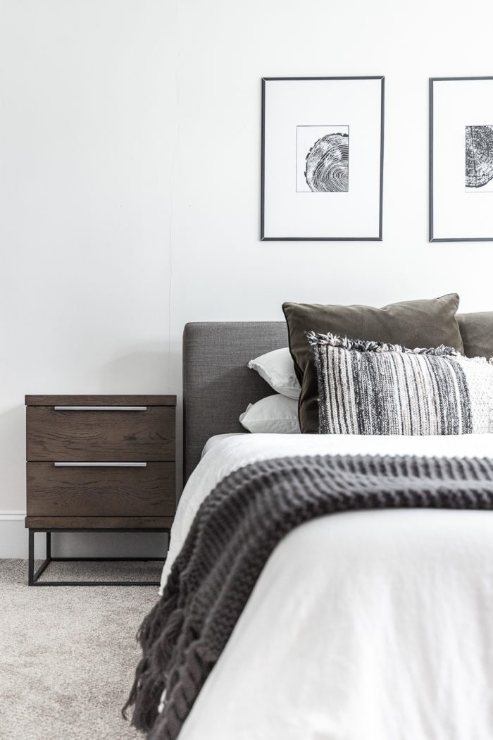 Master bedroom with gray headboard, minimalist design, black and white art, and white bedding. 
