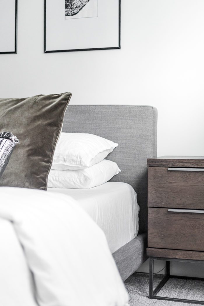 Gray upholstered headboard, velvet pillows and dark wood nightstand. 