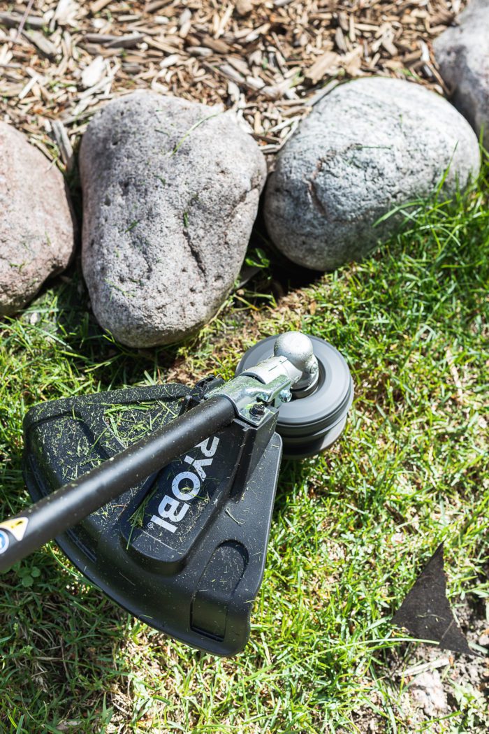 battery operated trimmer being used around landscaping rocks. 