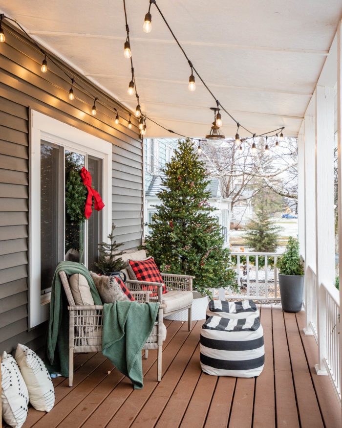 Classic Christmas Porch Decor with cozy pillows, poufs, and overhead cafe lighting. 