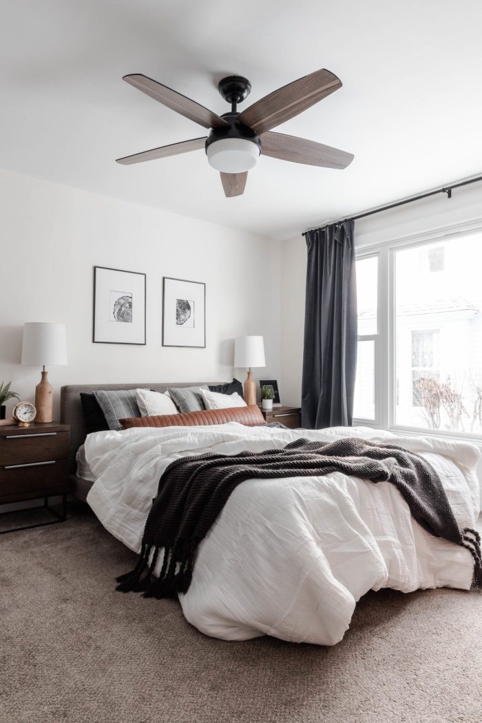 The Messy Look: featuring a lived in look. Queen size bed with a modern gray headboard, white bedding, dark gray accents and a leather lumbar pillow with layered white pillows and gray throw pillows. 