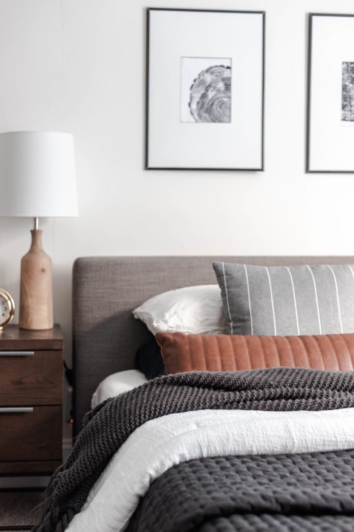 How to Make Your Bed like a Designer - The layered look: Queen size bed with a modern gray headboard, white bedding, dark gray accents and a leather lumbar pillow.