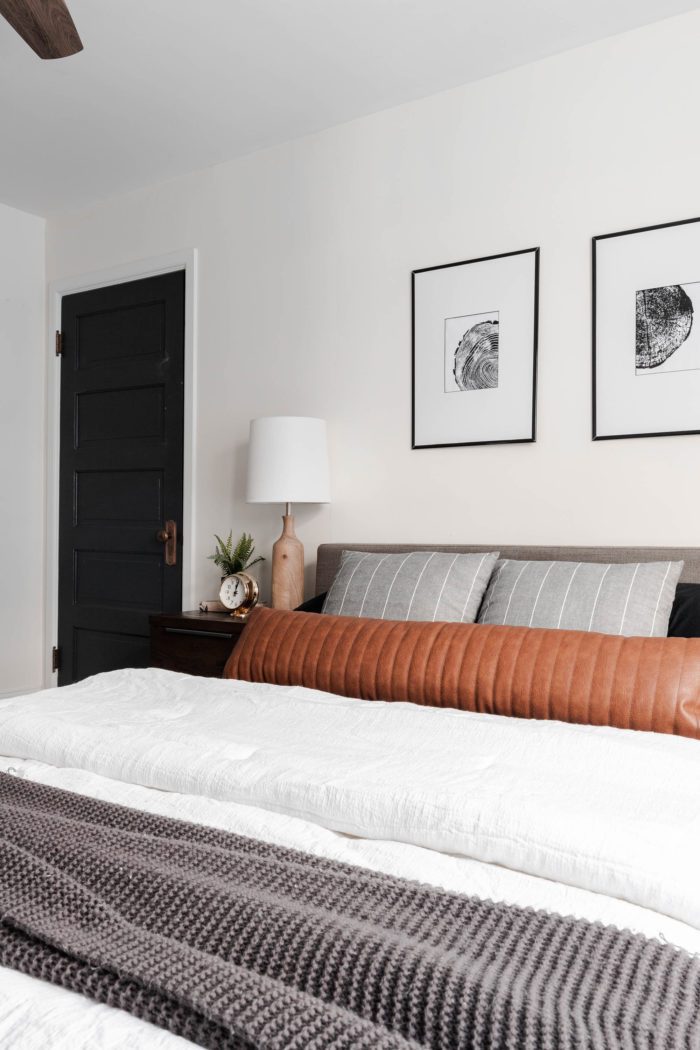 Queen size bed with a modern gray headboard, white bedding, dark gray accents and a leather lumbar pillow.