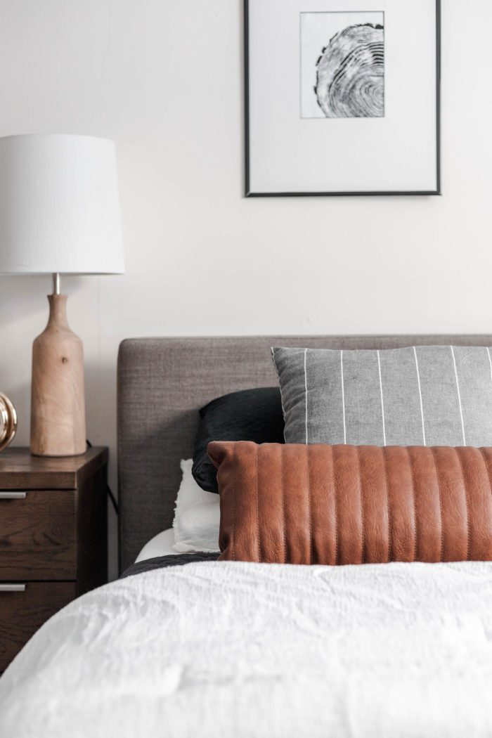 The Streamlined looks featuring clean lines. Queen size bed with a modern gray headboard, white bedding, dark gray accents and a leather lumbar pillow.